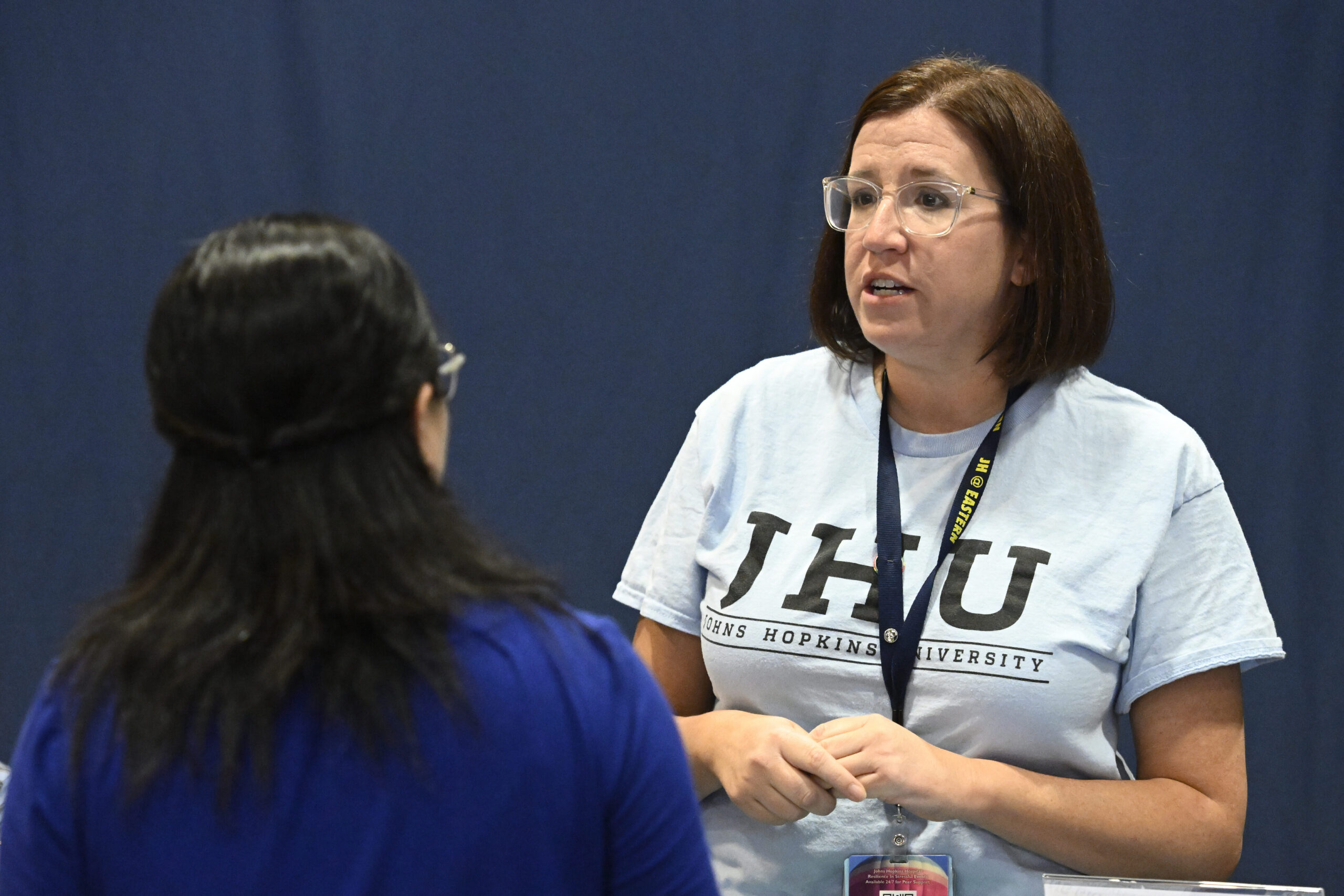 A woman wearing a blue shirt that says "JHU" talking to another woman at an event.